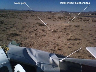 In the center of the screen, one can see the nose gear. To the right and on the near edge of the dirt road is the mark left by the initial impact of the nose.